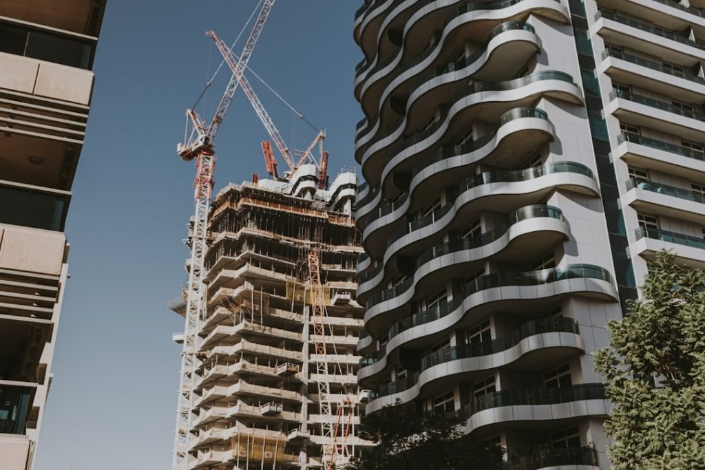 Construction of a high-rise building with cranes next to a modern curved apartment building